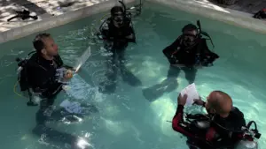 Candidatos a Divemaster e instructores revisando pizarras de entrenamiento en una sesión de aguas confinadas.