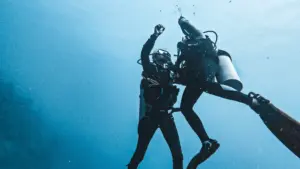 Candidatos a Divemaster practicando un ascenso controlado y asistencia de compañero en aguas azules cristalinas.